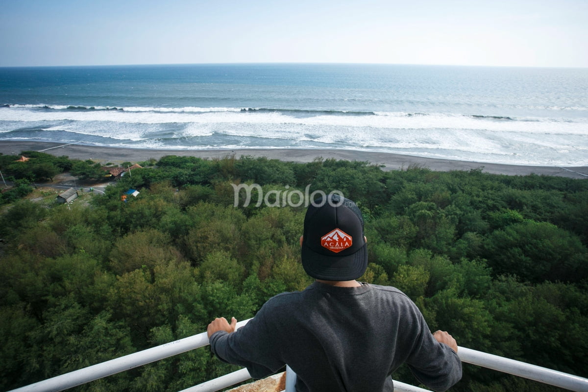 A visitor enjoying the view from the top of the lighthouse at Goa Cemara Beach.