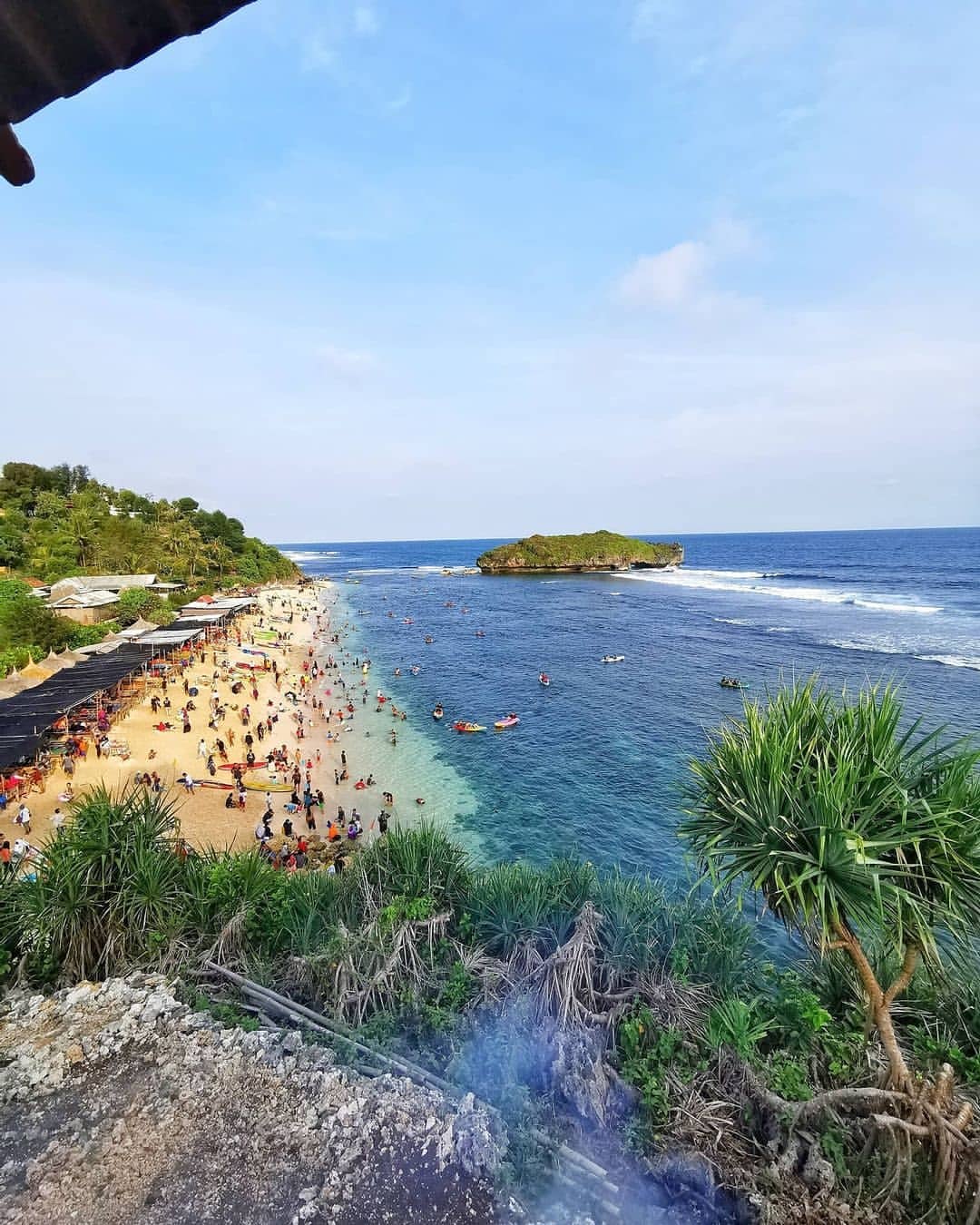 A view from above showing a busy Sadranan Beach with many visitors and a small island in the background.