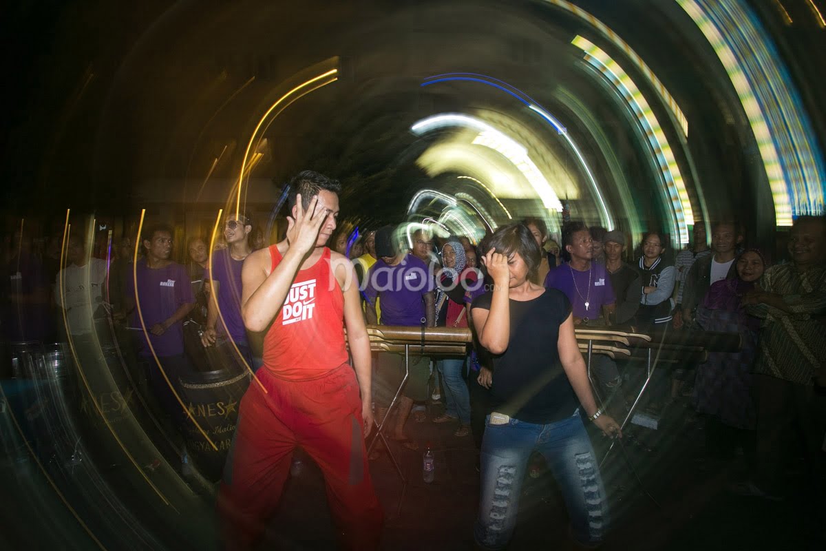 Two performers dancing during a calung music performance on Malioboro Street at night.