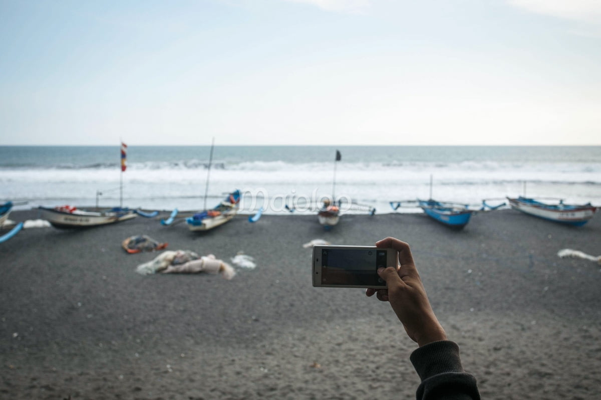 A person taking a photo of fishing boats lined up on the beach at Goa Cemara.