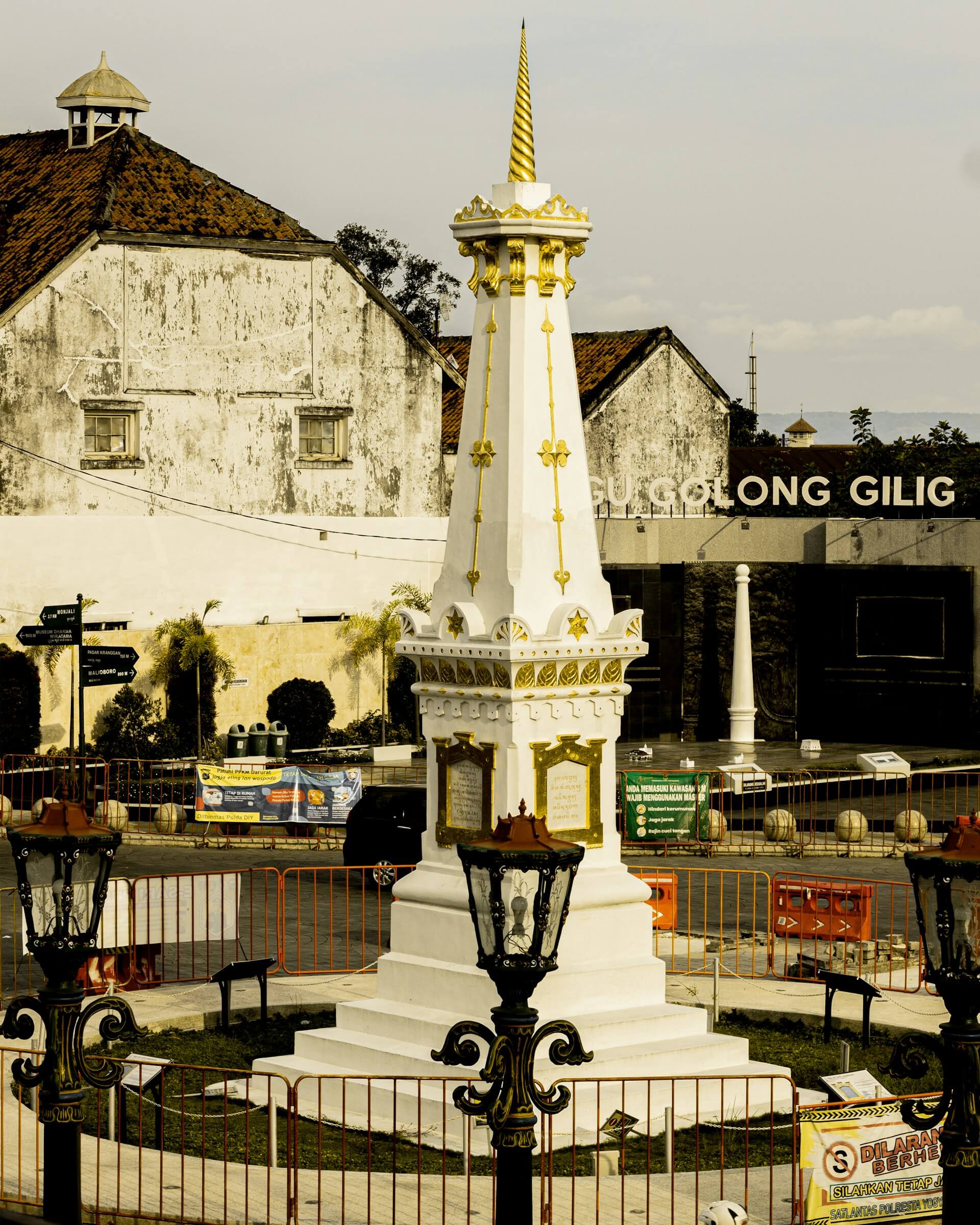 A close-up view of Tugu Yogyakarta, a white monument with golden accents, standing in front of an old building.