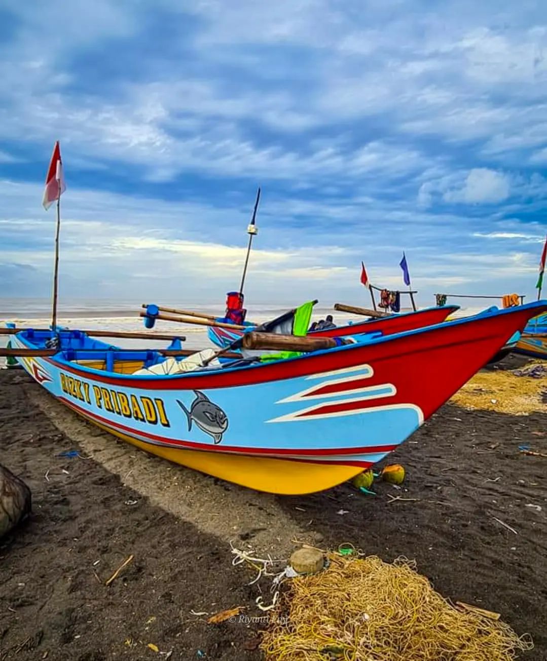 A colorful fishing boat on the black sand of Depok Beach.