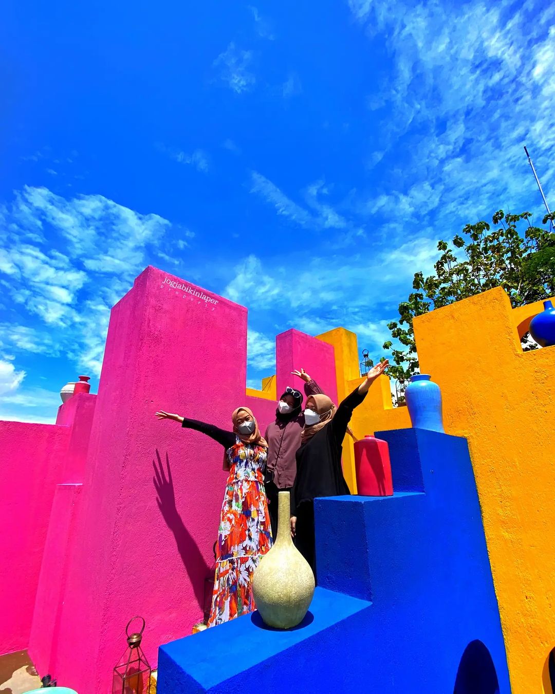 Three people posing in front of bright, colorful walls under a blue sky at Obelix Hills.