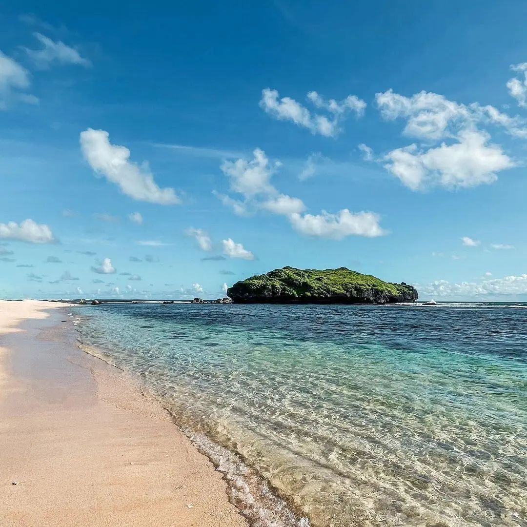 Clear shallow water at Sadranan Beach with a small green island under a blue sky.