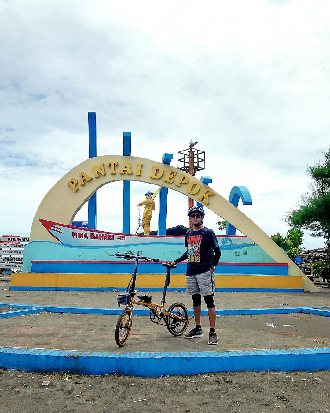 A cyclist stands with his bike in front of the Depok Beach sign.