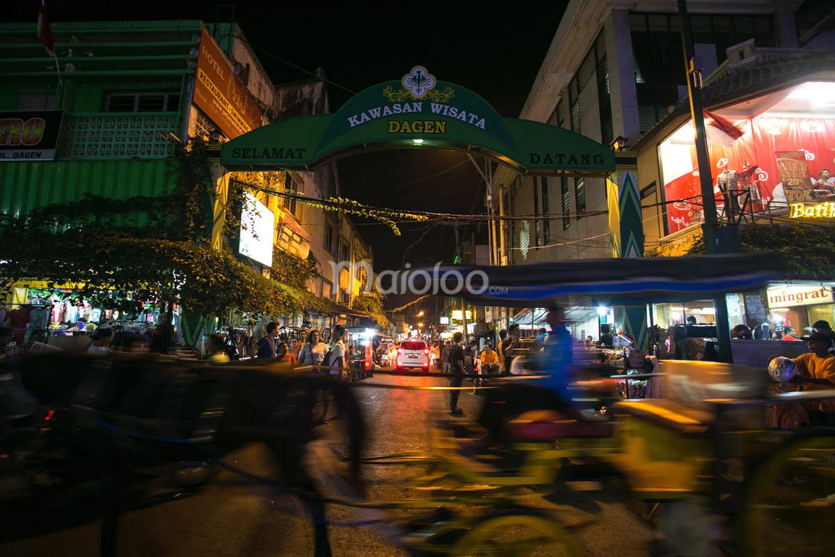 The Dagen Tourist Area gate illuminated at night with bustling street activity and horse-drawn carriages.