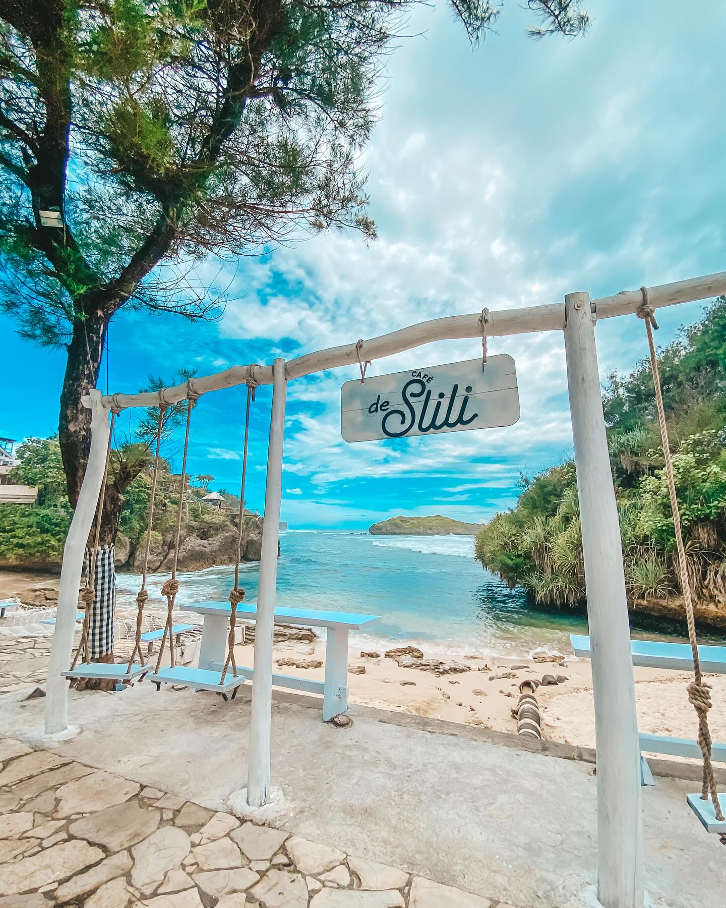 Swing set and a sign for de Slili Cafe with the ocean in the background at Slili Beach.