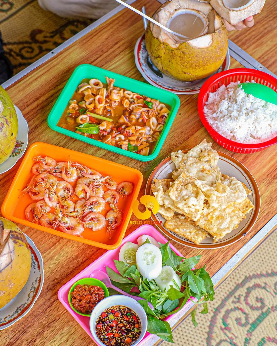 A table full of seafood dishes with rice, vegetables, and coconuts at Depok Beach.