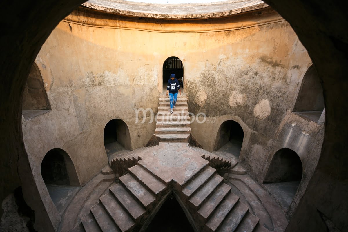 A person walks down the stairs inside the circular Sumur Gemuling at Taman Sari, Yogyakarta.