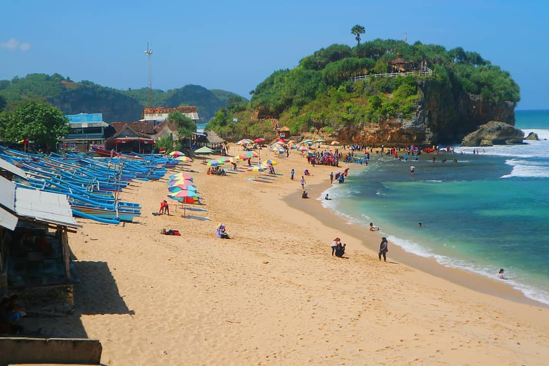 A sandy beach with colorful umbrellas, boats lined up, and people enjoying the water.