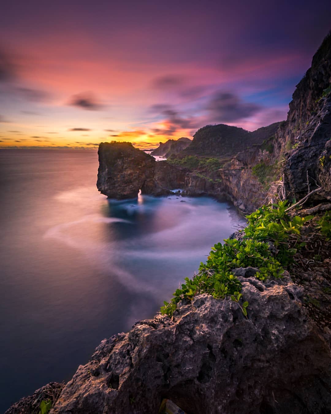 A vivid sunset at Ngungap Beach, coloring the sky with shades of purple and orange over the tall cliffs and sea.