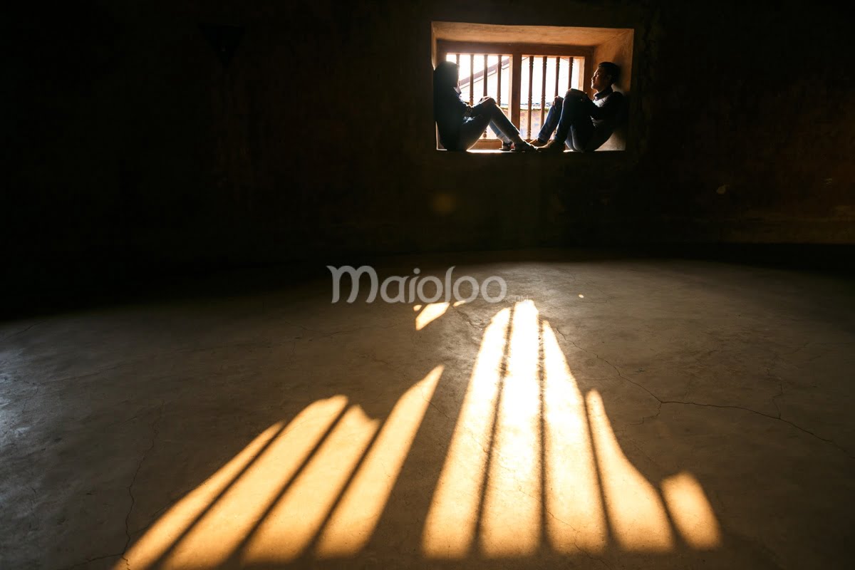 Two visitors sit in a window, with sunlight casting shadows on the floor inside Sumur Gemuling at Taman Sari, Yogyakarta.