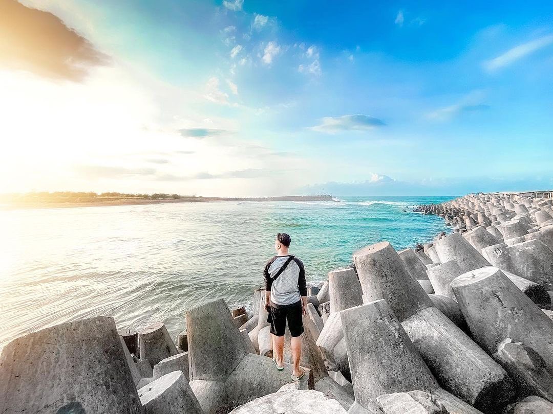 Man standing on concrete wave breakers at Glagah Beach looking at the sea.