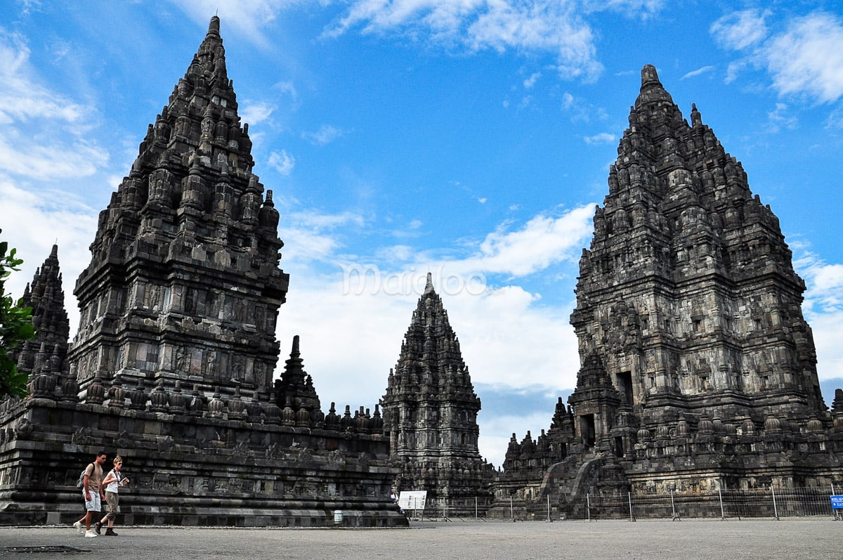 Tourists walking in front of Prambanan Temple on a sunny day.