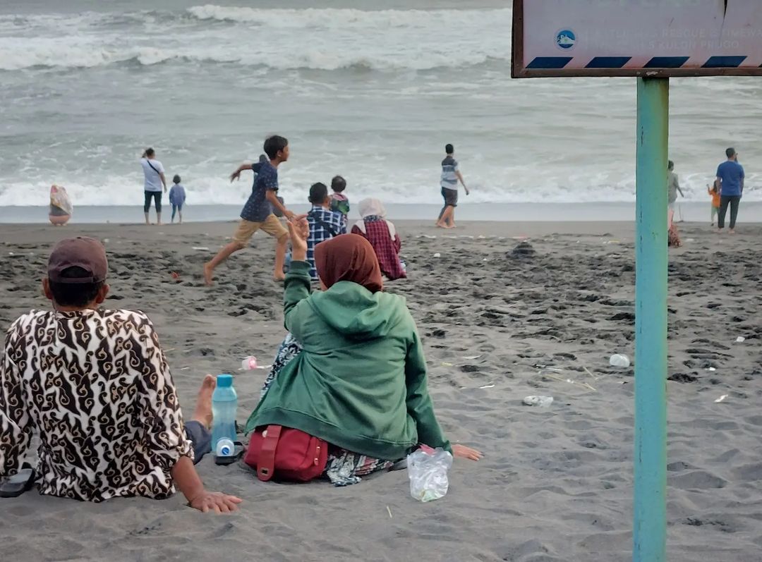 People sitting and playing on the sandy shore of Trisik Beach.