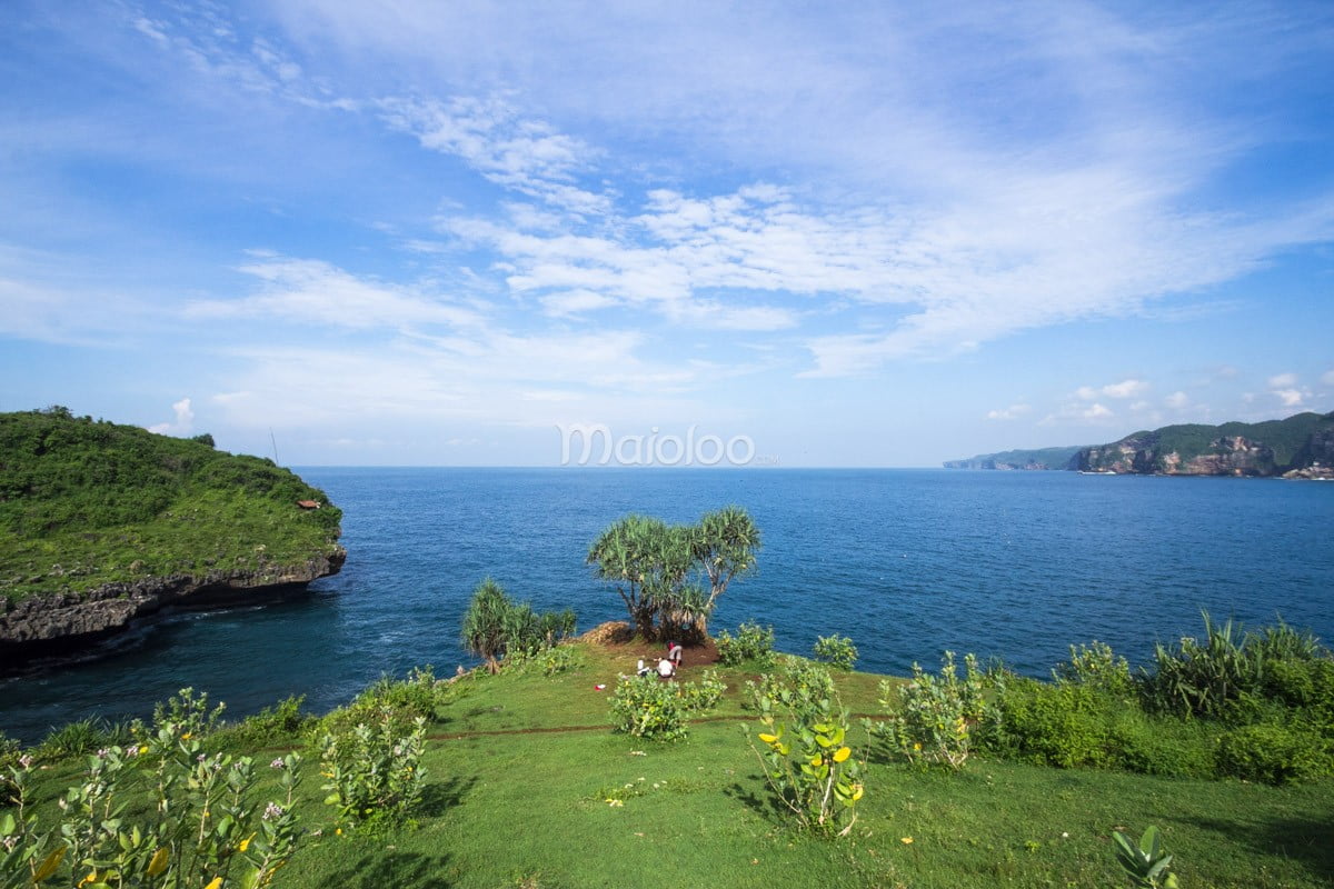 Visitors preparing fishing gear on a grassy cliff at Kesirat Beach, with the ocean in the background.