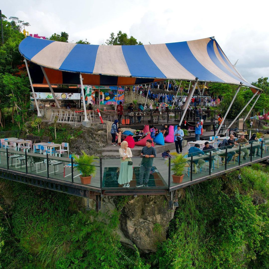 People enjoying drinks on a glass-floored terrace under a striped tent at Obelix Hills.