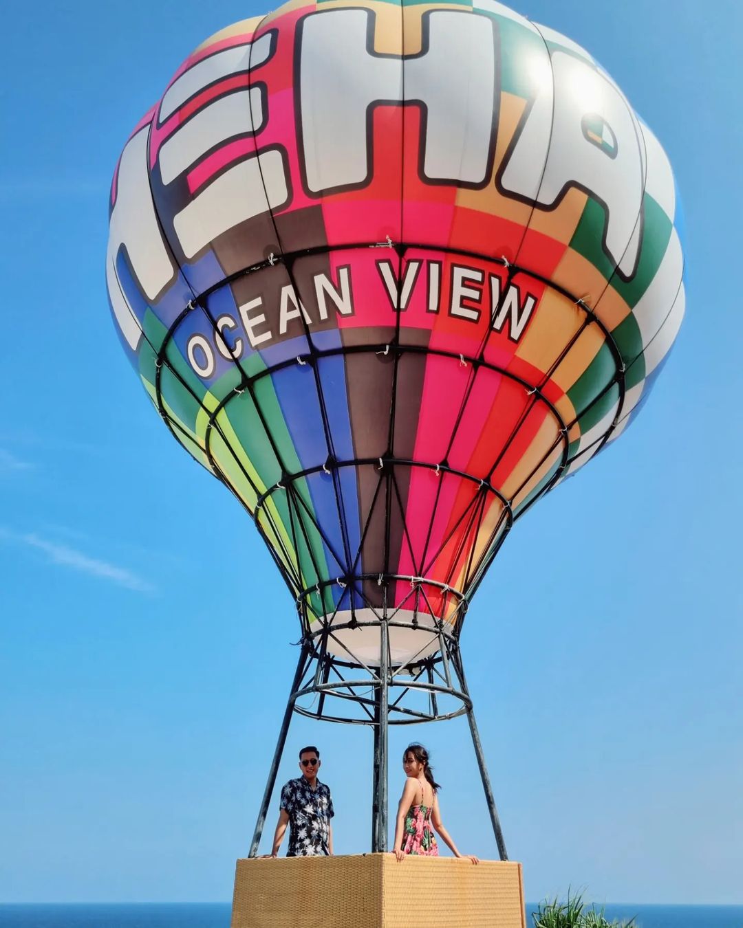 Two people standing in a colorful hot air balloon basket at HeHa Ocean View.