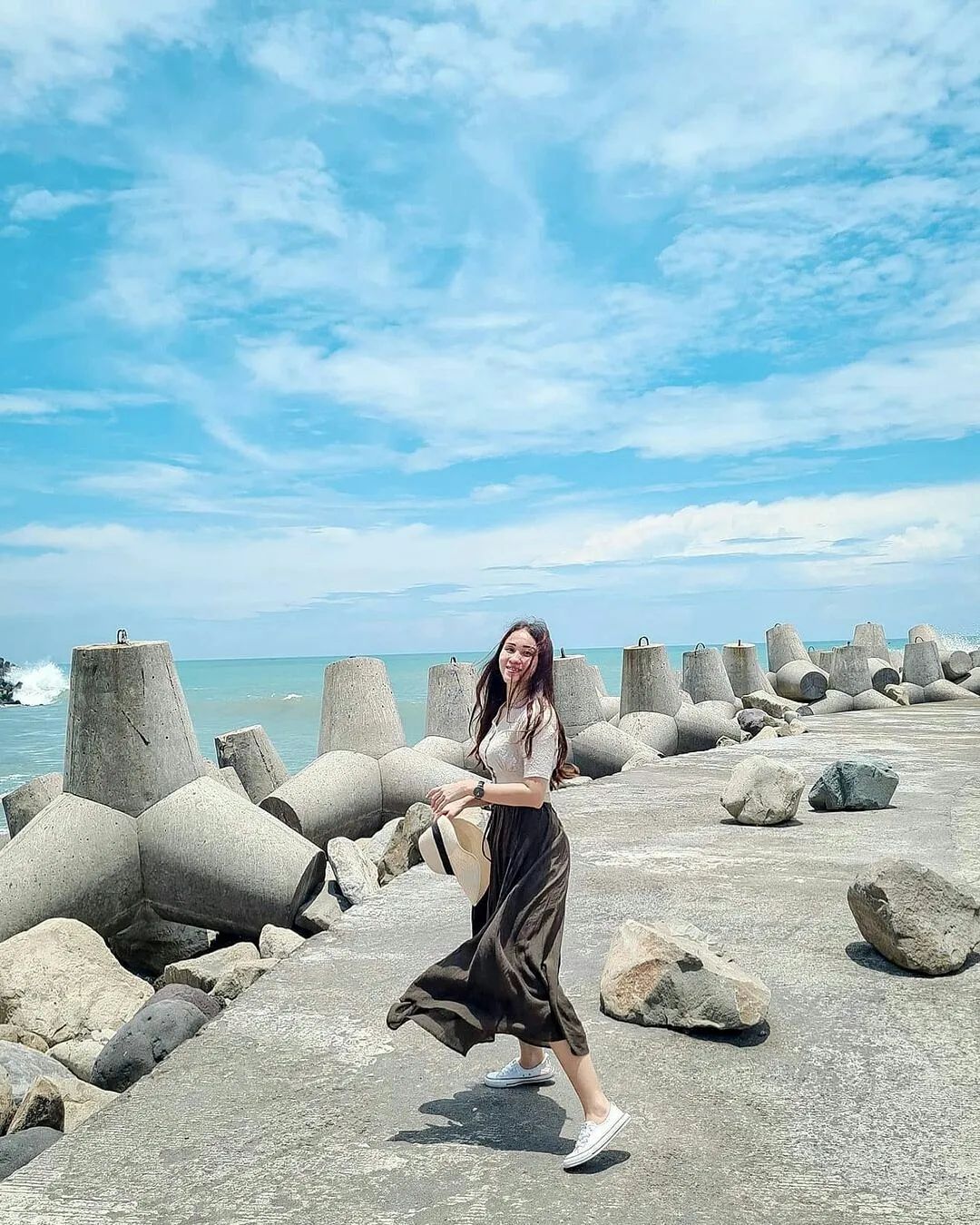 A woman smiling and walking on the wave breakers at Glagah Beach.