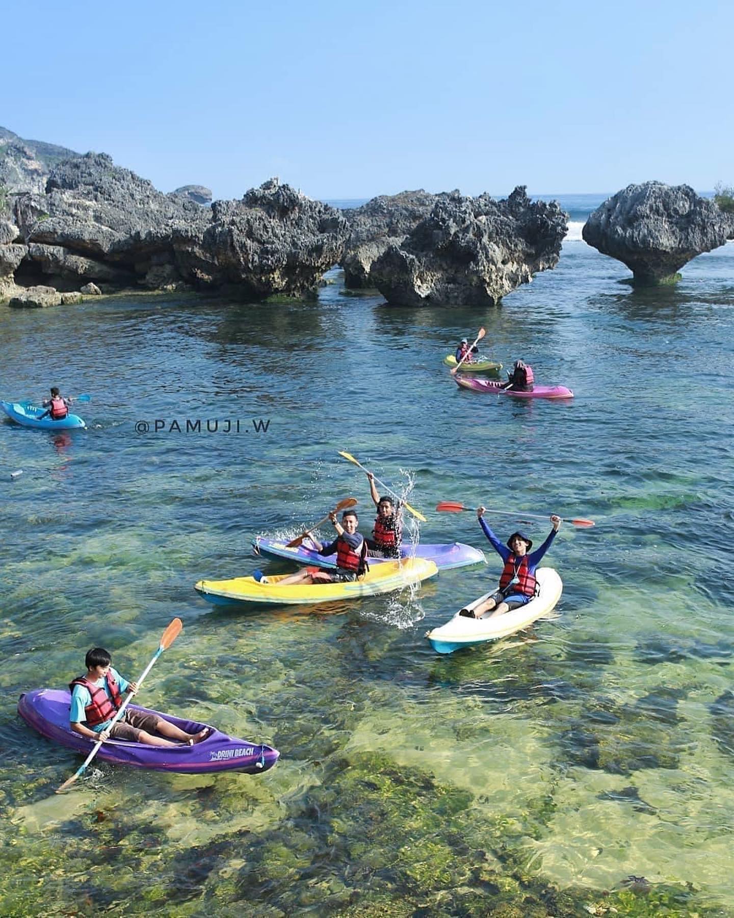 People kayaking in clear water near rocky formations.