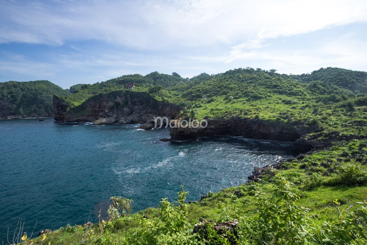 Green cliffs and blue ocean at Kesirat Beach under a clear sky.