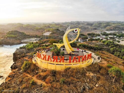 Aerial view of Krakal Beach sign with a large yellow fish statue and surrounding landscape.