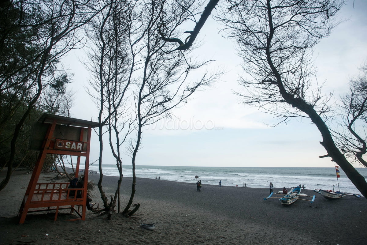 Lifeguard station at Goa Cemara Beach with people and boats on the shore.