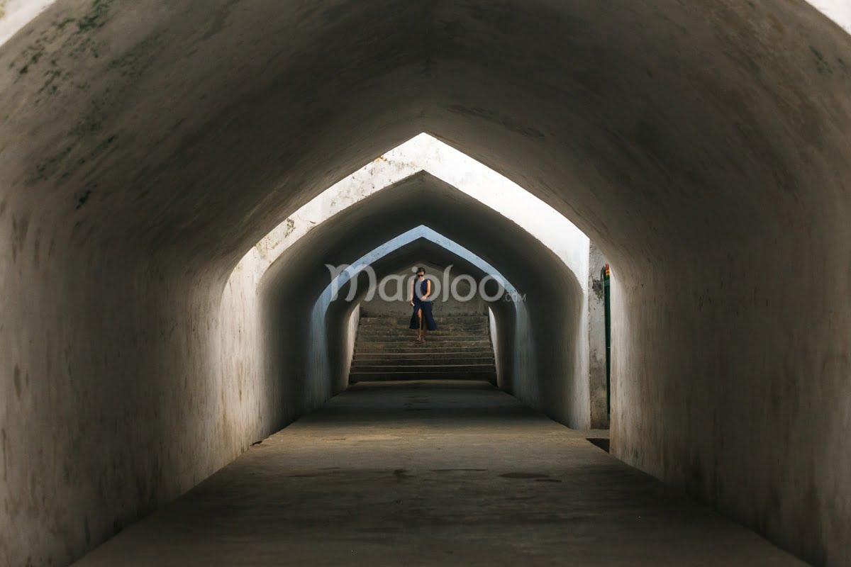 A person stands at the end of a dimly lit arched tunnel in Taman Sari, Yogyakarta.