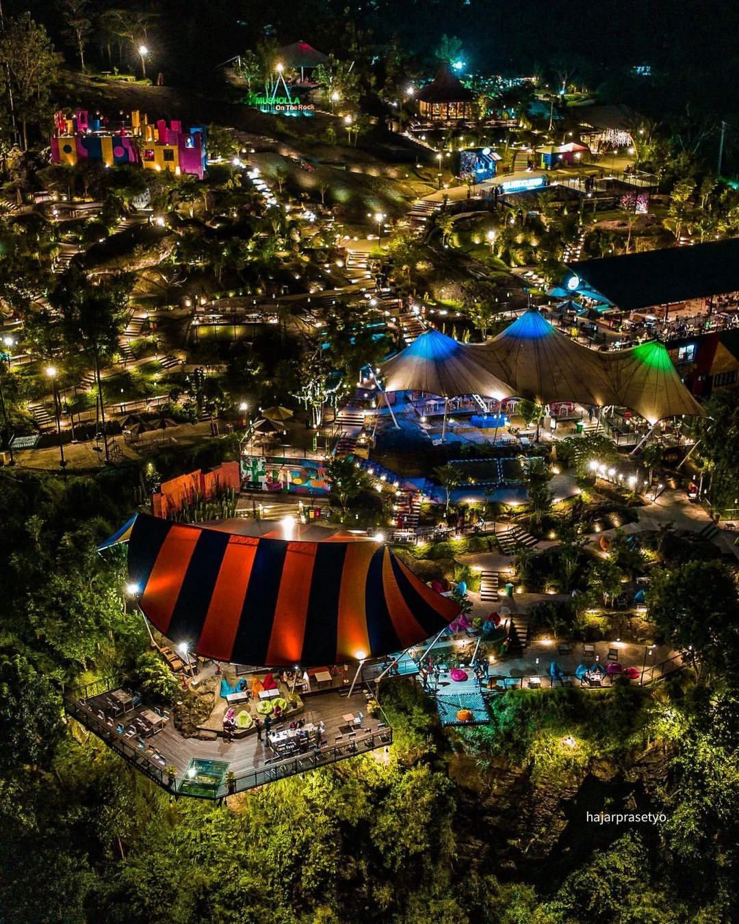 A dazzling night view of Obelix Hills with vibrant lights, colorful tents, and lush greenery.