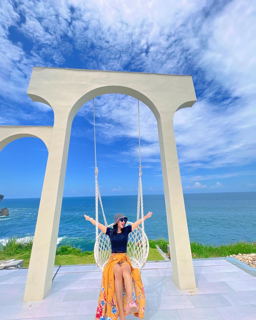 A woman sitting on a swing under white arches with an ocean view at HeHa Ocean View.