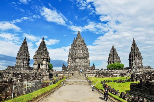 Central pathway leading to main spire of Prambanan Temple with blue sky above.
