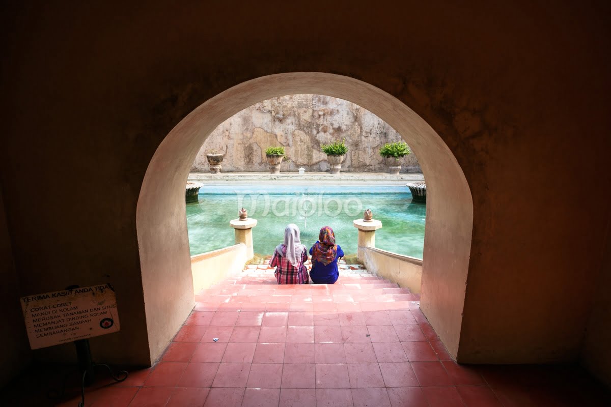 Two people sit on steps leading to the Umbul Binangun pool at Taman Sari, Yogyakarta.