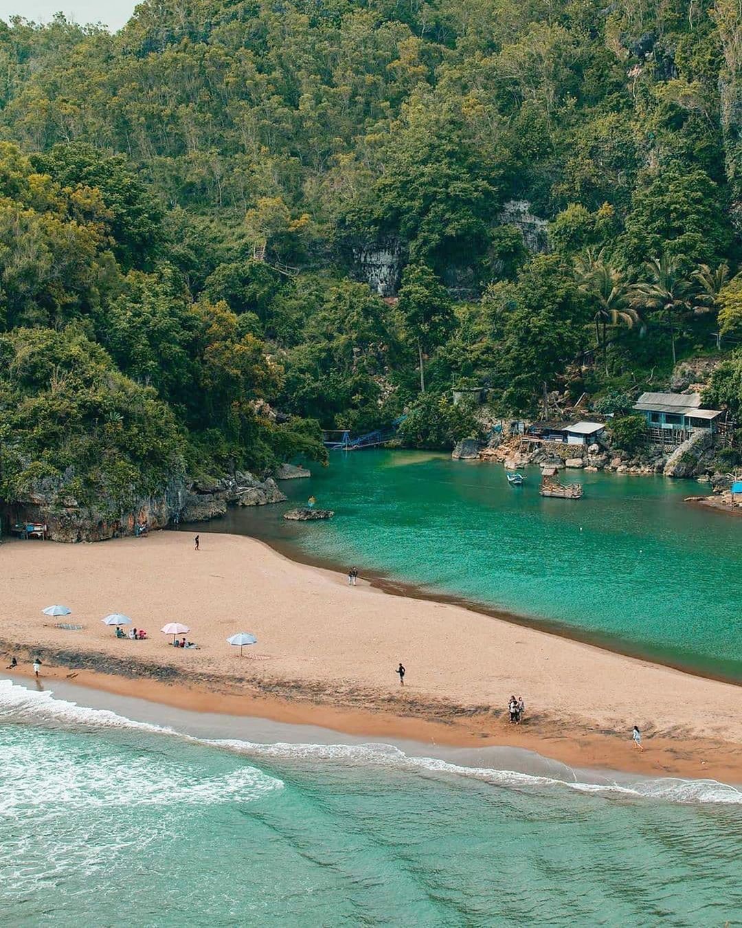 Serene view of Baron Beach with a sandy shore, turquoise water, and lush green hills.