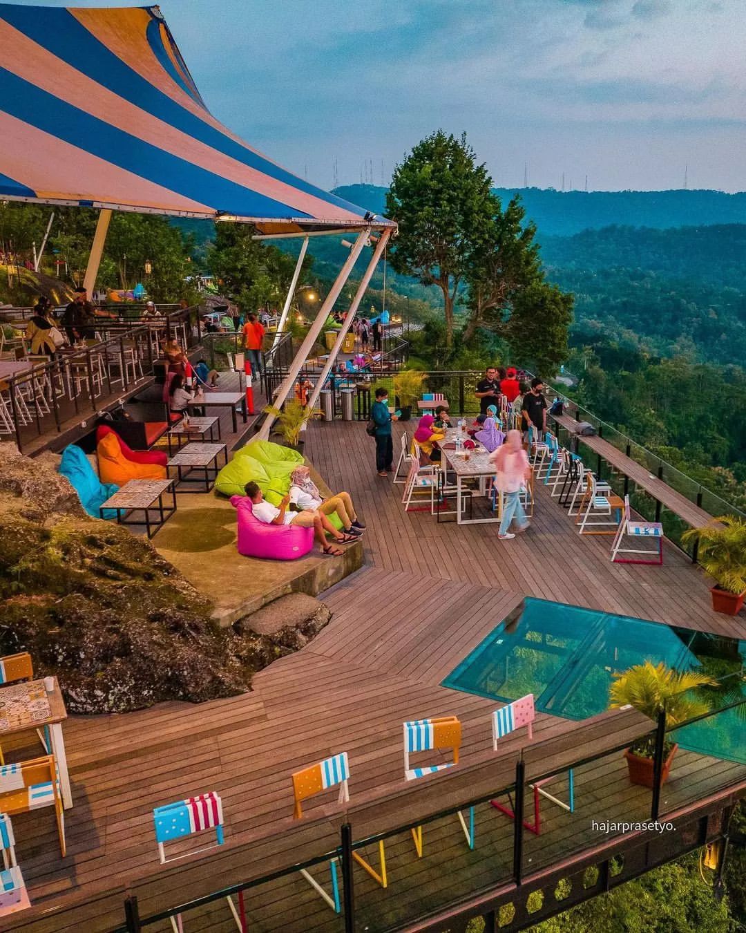 People relaxing and dining under a striped tent at Obelix Hills with a scenic view of lush green hills.