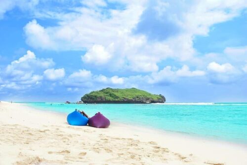 Two people relax on colorful inflatable loungers on Sadranan Beach with a small green island in the background.