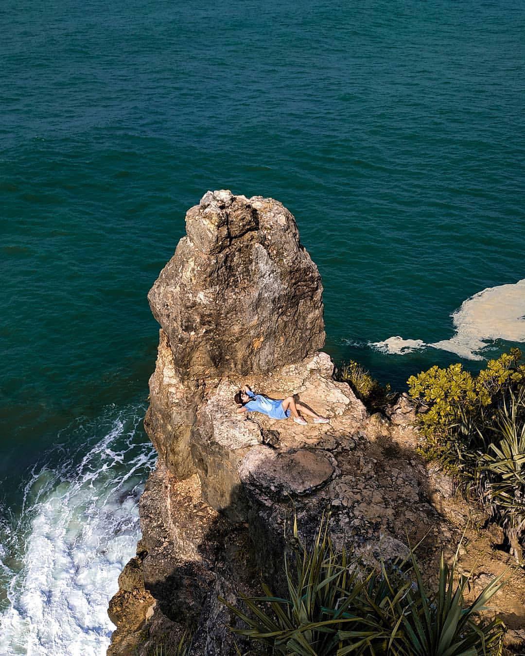 A person relaxing on a rocky cliff overlooking the ocean at Ngetun Beach.