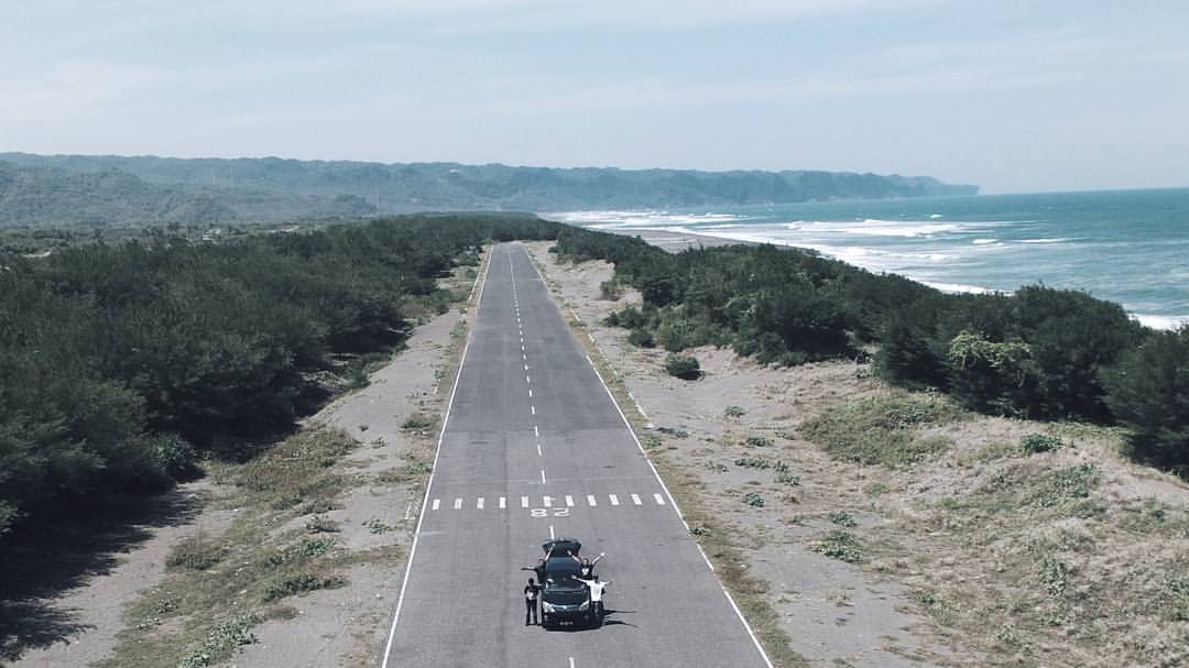 A car parked on a runway near Depok Beach with ocean and greenery in the background.