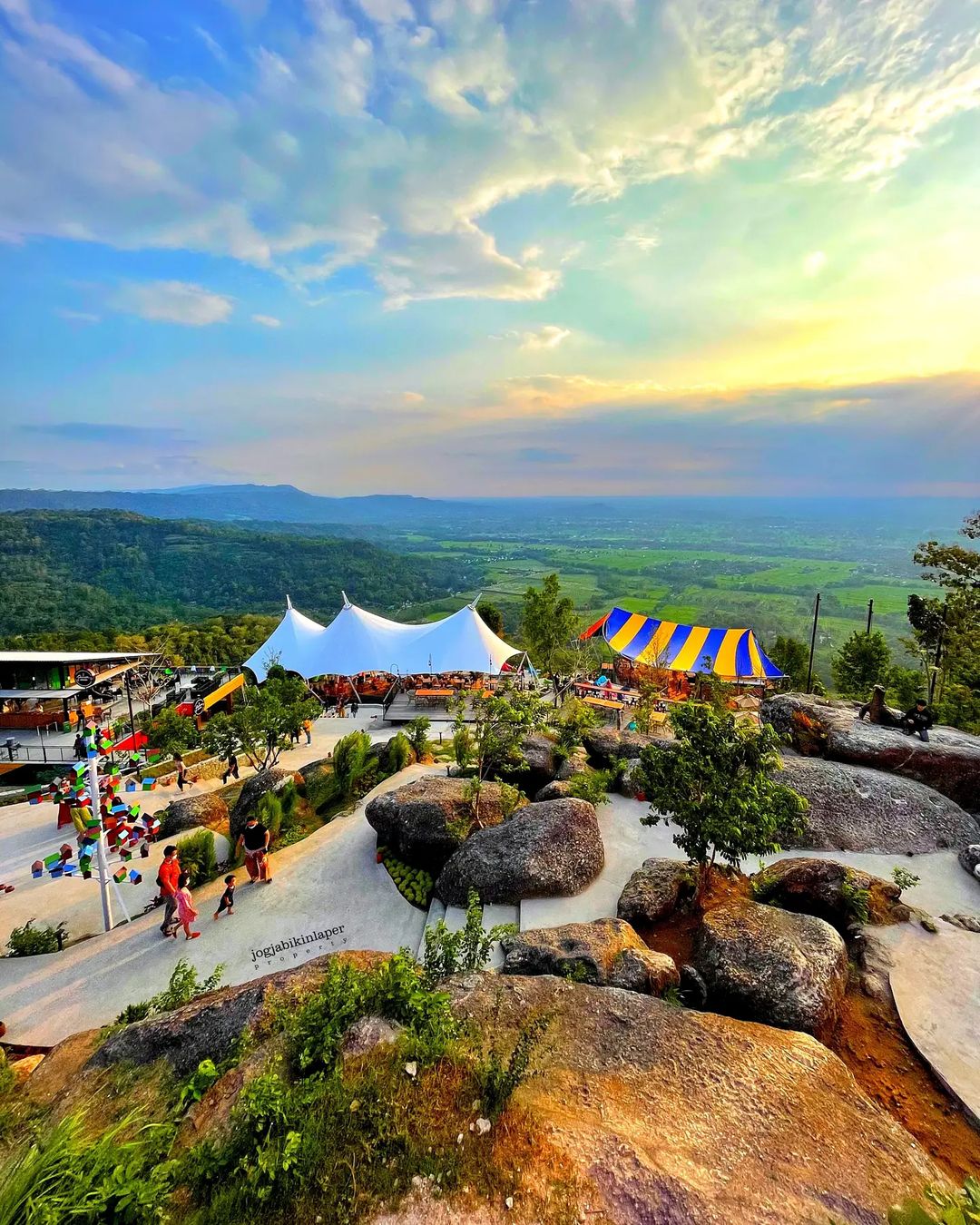 A scenic view of Obelix Hills with colorful tents, large rocks, and lush green landscapes under a vibrant sky.