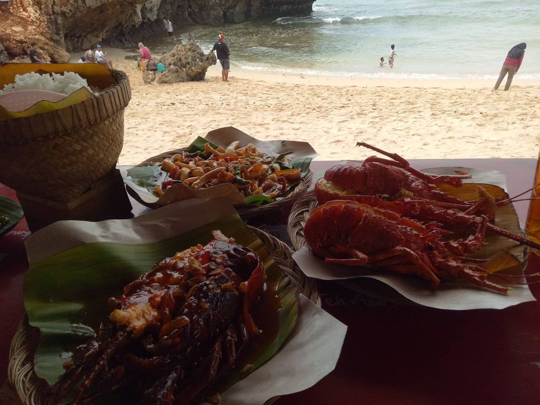 Plates of seafood and rice served on a table at Sundak Beach with people enjoying the beach in the background.