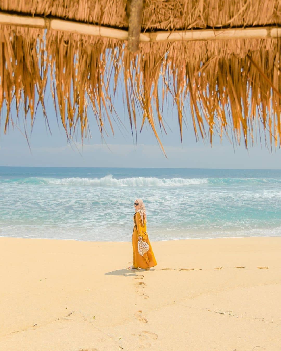 Woman in a yellow dress walking on the sandy shore of Watulawang Beach.