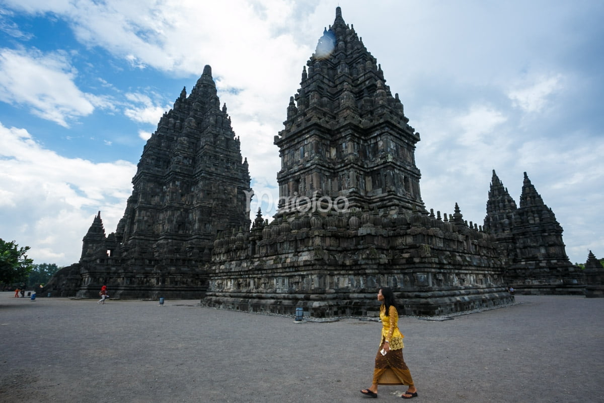 A woman in traditional clothing walking in front of Prambanan Temple.