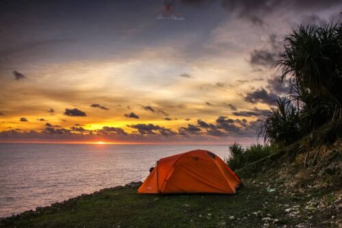 An orange tent on a cliff overlooking the ocean at sunset.