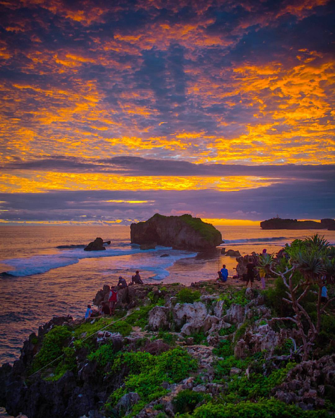 Group of people sitting on rocky cliffs at Sundak Beach enjoying the colorful sunset.