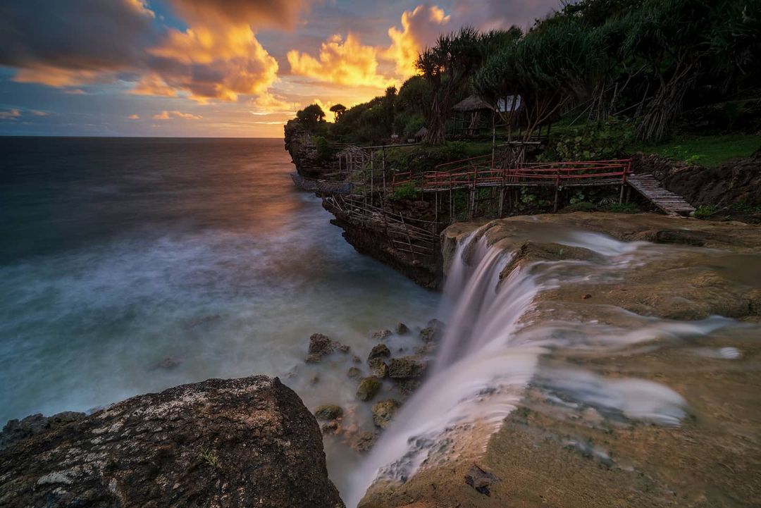 unset view at Jogan Beach with a waterfall flowing into the ocean and dramatic clouds in the sky.