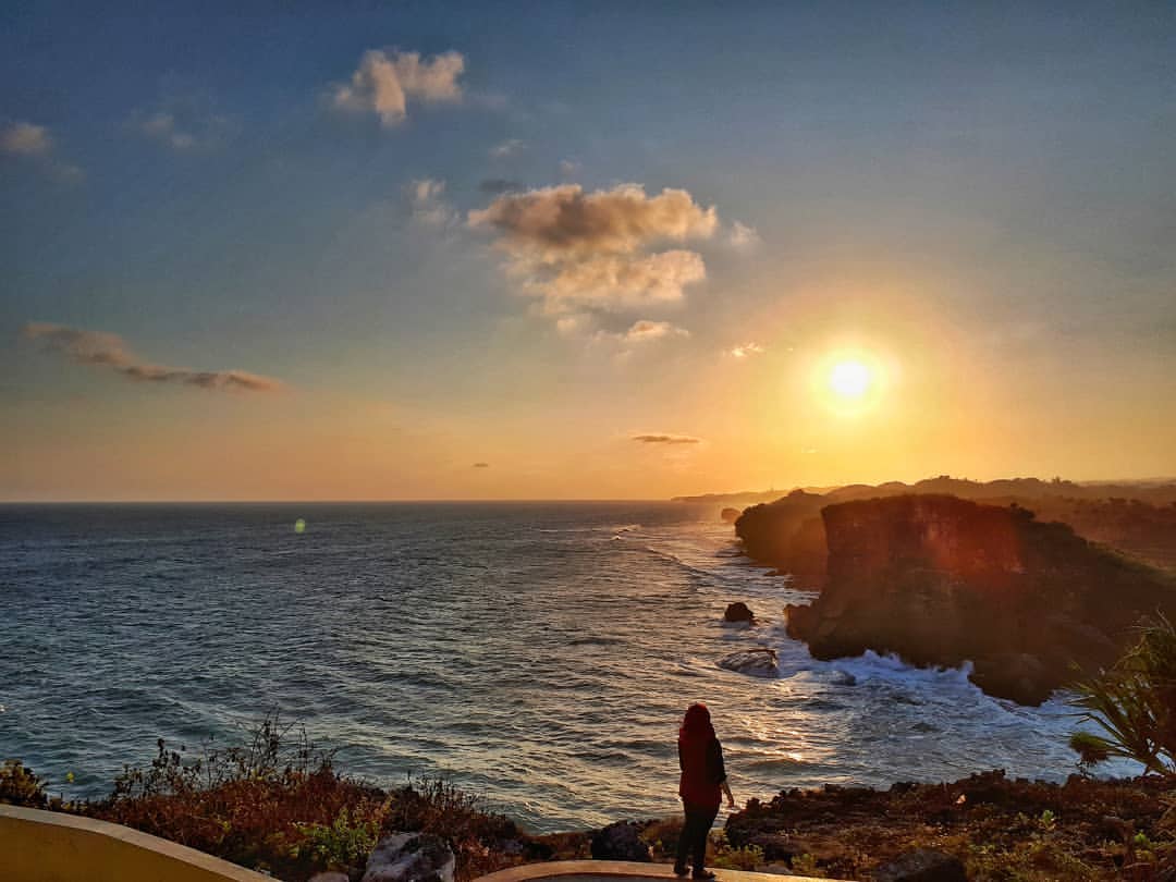 A person standing on the cliffside of Krakal Beach, watching the sunset over the ocean.