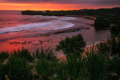 Beautiful sunset over Sundak Beach with waves gently crashing onto the shore and lush greenery in the foreground.