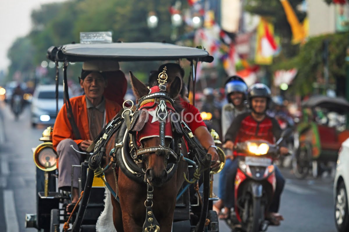 A horse-drawn carriage and motorbike riders on Malioboro Street.