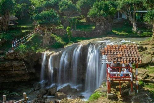 Waterfall at Jogan Beach flowing into the ocean with a small wooden shelter nearby.