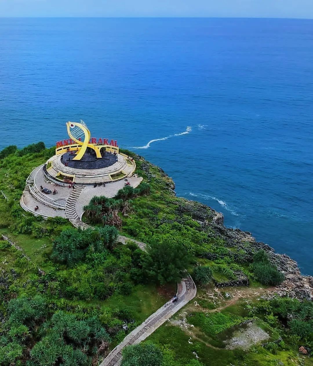 Aerial view of Krakal Beach's yellow fish statue on a green cliff with a blue ocean backdrop.