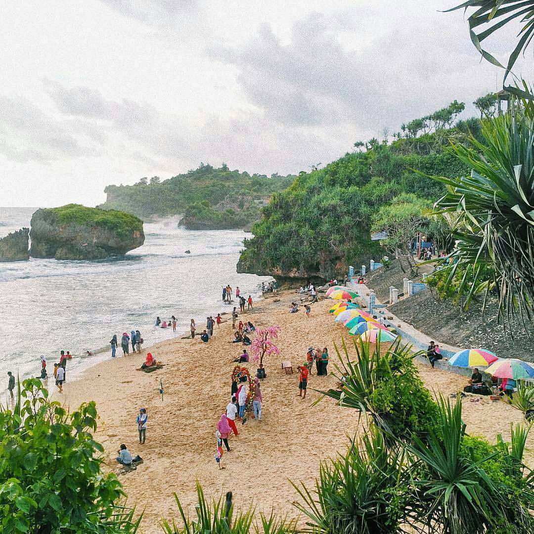 People enjoying a day at Kukup Beach with colorful umbrellas and green hills in the background.